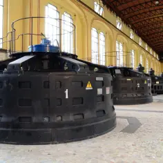 Wnętrze elektrowni z rzędem dużych, czarnych turbin wodnych.