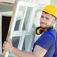 Budowlaniec w żółtym kasku usuwa stare okno.