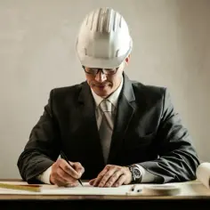 Inżynier w kasku i garniturze pisze przy biurku z planami i miarką.