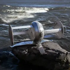 Metalowa turbina wodna na skale nad rwącą rzeką.